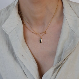 Détail d'un collier double rang en titane doré avec pendentif ovale en pierre noire
