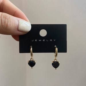 Close-up of gold heart drop earrings with black zircon stones and polished finish
