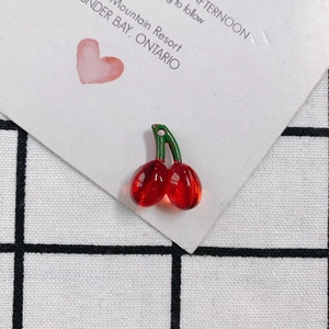 Close-up of a translucent red cherry pendant with a green stem on a white heart card