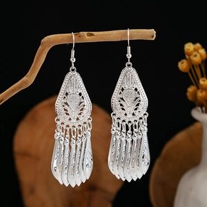 Detail of silver ethnic drop earrings featuring hollow leaf carving and long tassel accents