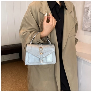 Détail du sac argenté à motif crocodile et fermoir doré porté avec un trench-coat