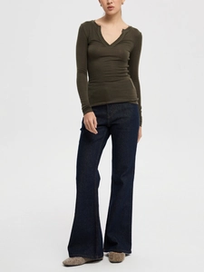 Detail of dark green slim fit V-neck knit top and flare jeans on a studio model