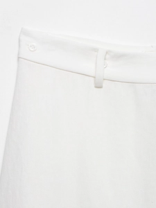 Detail of white satin pants featuring a waist button and textured fabric weave