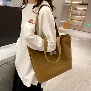 Brown thickened canvas tote bag with fashion tag carried by a model in a minimal setting