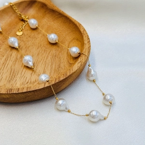 Detailed close-up of Baroque pearl necklace with gold chain on a wooden tray