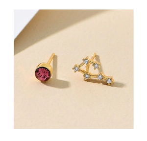 Detailed close-up of asymmetrical gold-plated stud earrings with pink gemstone and constellation design