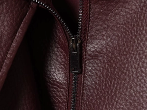 Détail macro d'une veste en cuir bordeaux grainé avec fermeture éclair métallique