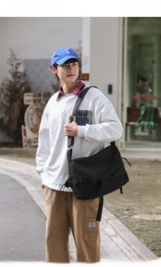 Close-up of a large black canvas messenger bag with a buckle and adjustable wide strap
