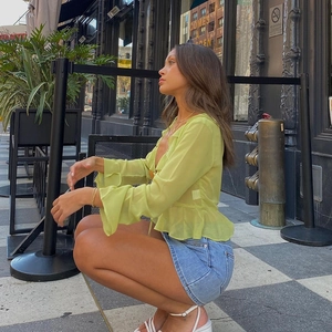 Detail of light green ruffle chiffon top with tie-up V-neck and denim mini skirt
