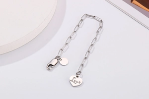 Detail of silver chain bracelet featuring a heart Love charm and circular metal disk