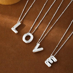 Silver stainless steel balloon letter necklaces spelling LOVE on brown velvet background