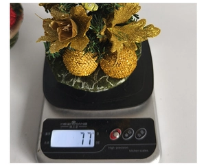 Mini gold Christmas tree ornament on kitchen scale showing product weight of 77g
