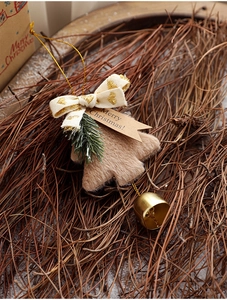 Detail of plush brown Christmas tree ornament with bell, pine needles and a gift tag
