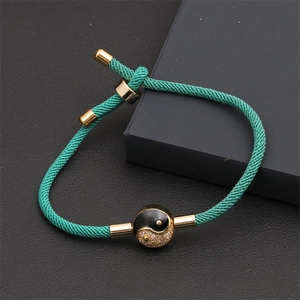 Detail of green woven bracelet with gold Yin Yang charm and adjustable cord on black display