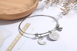 Detail of silver adjustable bangle with moon star charms on a wooden tray with flowers