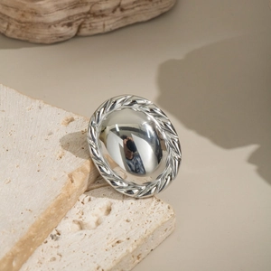 Detailed view of silver oval lace mirror ring resting on natural beige travertine stone