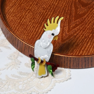 Handcrafted acrylic cockatoo bird brooch with yellow crest perched on a leafy branch