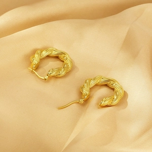 Detailed view of gold twisted rope hoop earrings resting on elegant champagne silk fabric