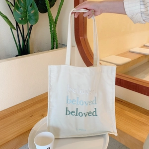 Détail du texte brodé 'beloved' sur un sac fourre-tout en toile crème à anses