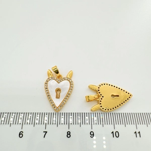 Golden heart pendant with white shell inlay and rhinestones shown against a ruler scale