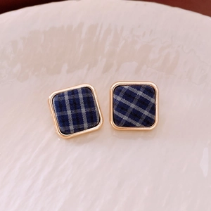 Vue macro de boucles d'oreilles carrées en tissu à carreaux bleu avec bord doré