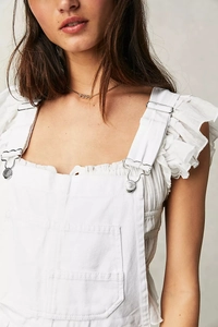 Detail of white denim overalls with ruffle sleeves and metallic buckles on the straps