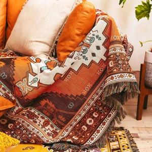 Bohemian woven camping blanket with geometric patterns and fringe edges on a sofa
