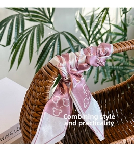 Close-up of a pink heart-printed silk twilly scarf tied to a woven basket bag handle