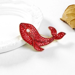 Détail de la broche baleine avec cristaux rouges et perle blanche sur monture dorée