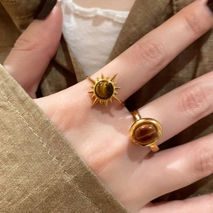 Vintage golden open rings with tiger eye stones worn by a model on a brown background