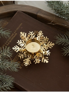Close-up of golden snowflake tea light holder on vintage books with pine branches