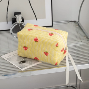 Detail of quilted yellow checkered makeup bag with strawberry prints and white ribbon zip