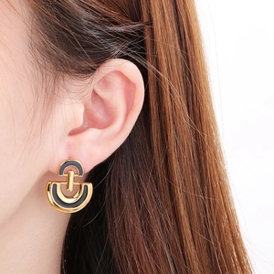 Close-up of golden D-shaped stainless steel earrings with black enamel inlay on model