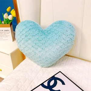 Gros plan d'un coussin en peluche cœur bleu avec texture d'écailles sur un lit doux