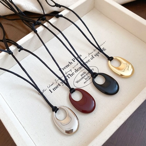 Détail de quatre pendentifs gouttes en or, argent, noir et bordeaux sur cordons noirs
