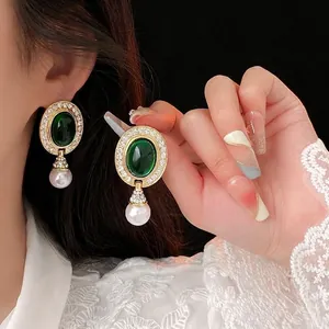 Detail of vintage gold earrings with green gemstone and hanging white pearl on model