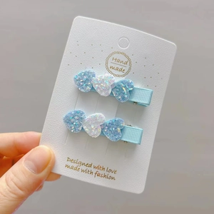 Detail of two handmade glitter heart hair clips in blue and silver on a display card