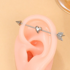 Close-up of silver punk heart and arrow industrial barbell piercing on an ear model