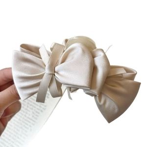 Elegant cream satin bow hair claw clip for women's bun hairstyle on white background