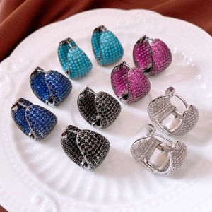 Close-up of wide U-shaped hoop earrings set with colorful cubic zirconia on a white plate