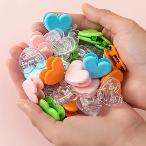 Close-up of colorful heart-shaped plastic clips being held in hands on pink background