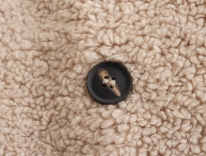 Détail du tissu polaire sherpa beige avec un bouton en résine marron foncé élégant