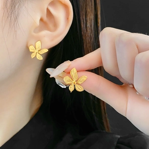 Macro detail of gold flower stud earrings in stainless steel on ear and fingers