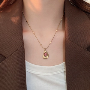 Close-up of a pink gemstone oval necklace on a gold beaded chain worn by a model