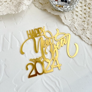 Close-up of golden acrylic Happy New Year 2024 cake topper with reflective finish
