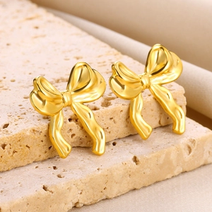 Close-up of polished 18K gold bow stud earrings on a stone base with silk
