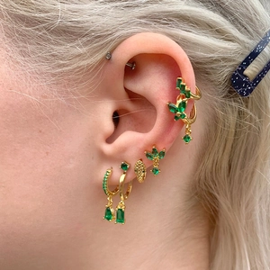 Macro shot of gold earrings set with emerald green gems including butterfly and teardrop charms