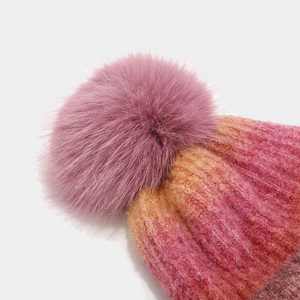 Close-up of a fluffy pink faux fur pompom and gradient knit texture on a winter hat