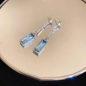 Elegant silver earrings with blue rectangle zircon stones and sparkling tassels on mirror