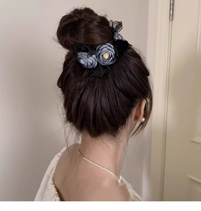 Detail of dark blue fabric flower hair claw clip on model's bun with golden accents